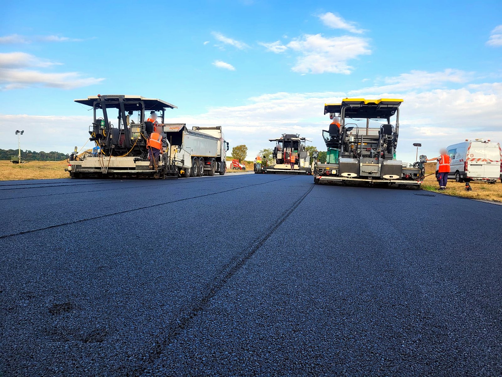 Trois finisseurs au travail sur un grand tapis d'enrobé
